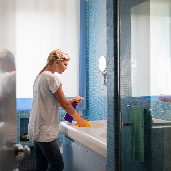 woman wearing cleaning gloves sprays vanity countertop in bathroom