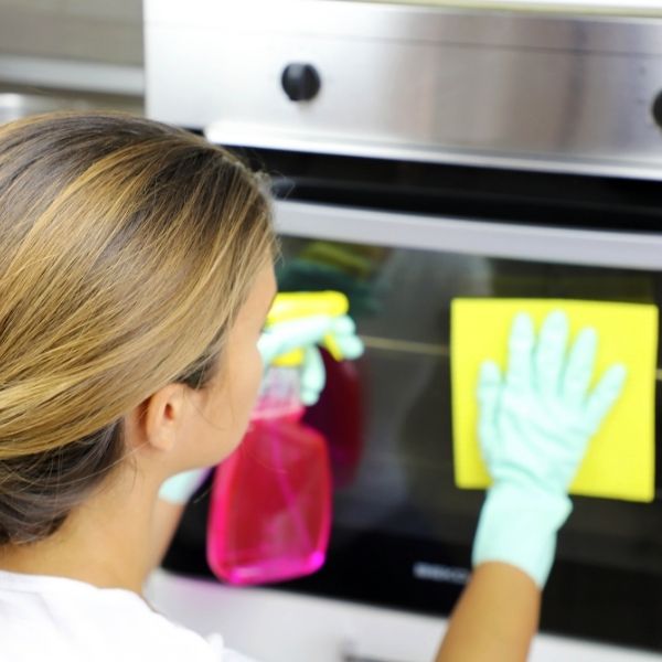 woman sprays cleaner on oven door