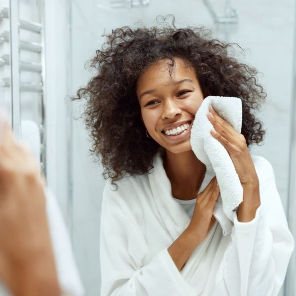 woman wearing bathrobe smiles while drying face with towel