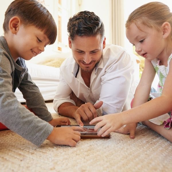 dad and kids lay on floor to play game on tablet